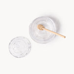 Gewurzhaus glass beehive-shaped honey jar with a matching lid and a small wooden honey dipper.
