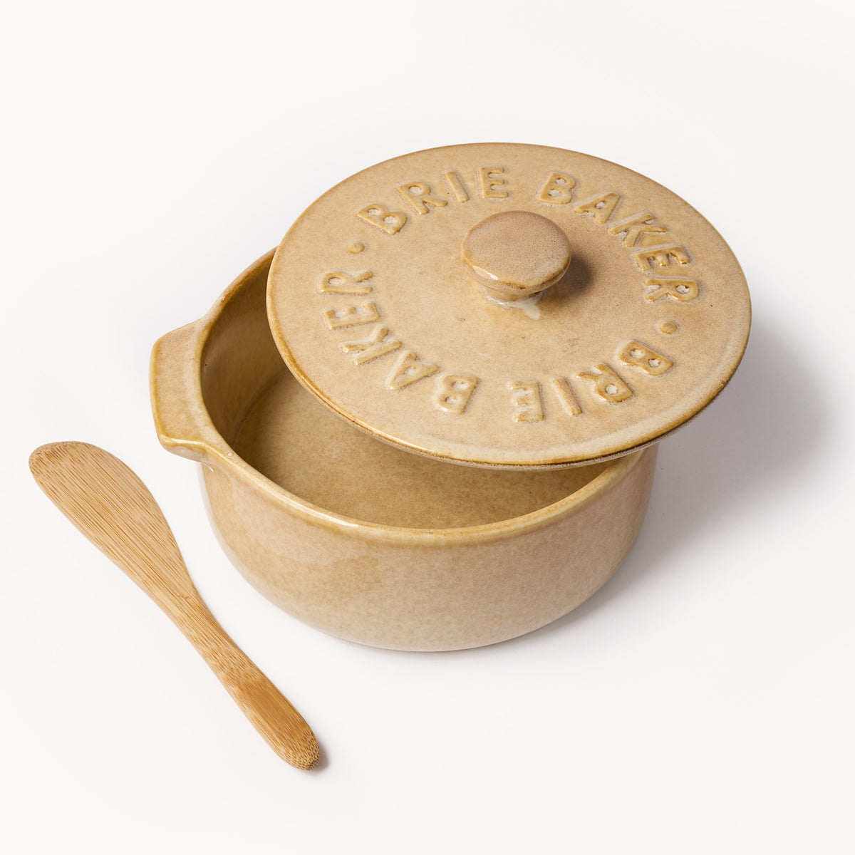 A beige ceramic Brie Bakker lidded pot with a matching wooden spatula, photographed on a clean white background.