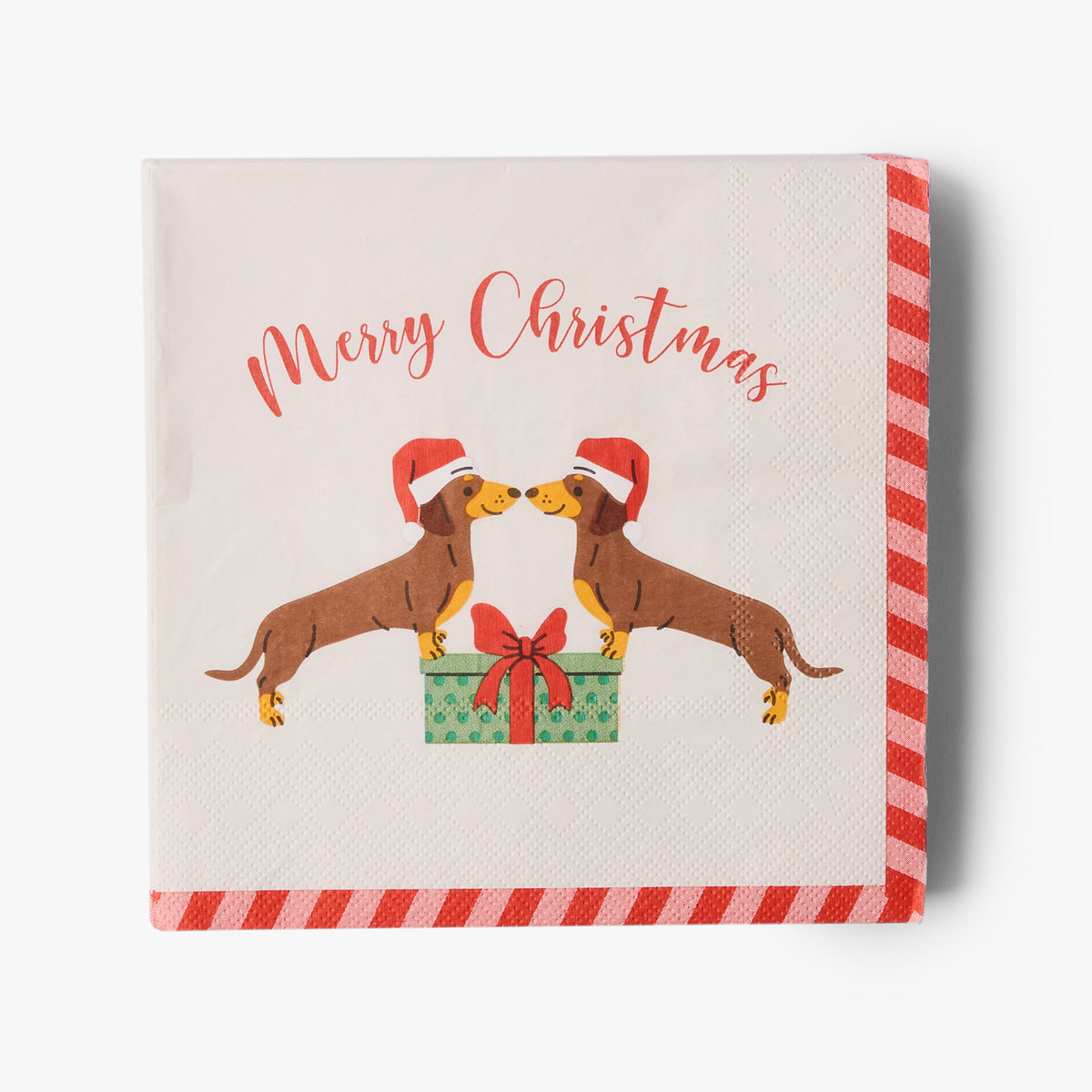 A square Christmas paper napkin with a white background, featuring a red and white striped border, the text 'Merry Christmas' in red script, and an illustration of two dachshunds wearing Santa hats standing on a green gift box.