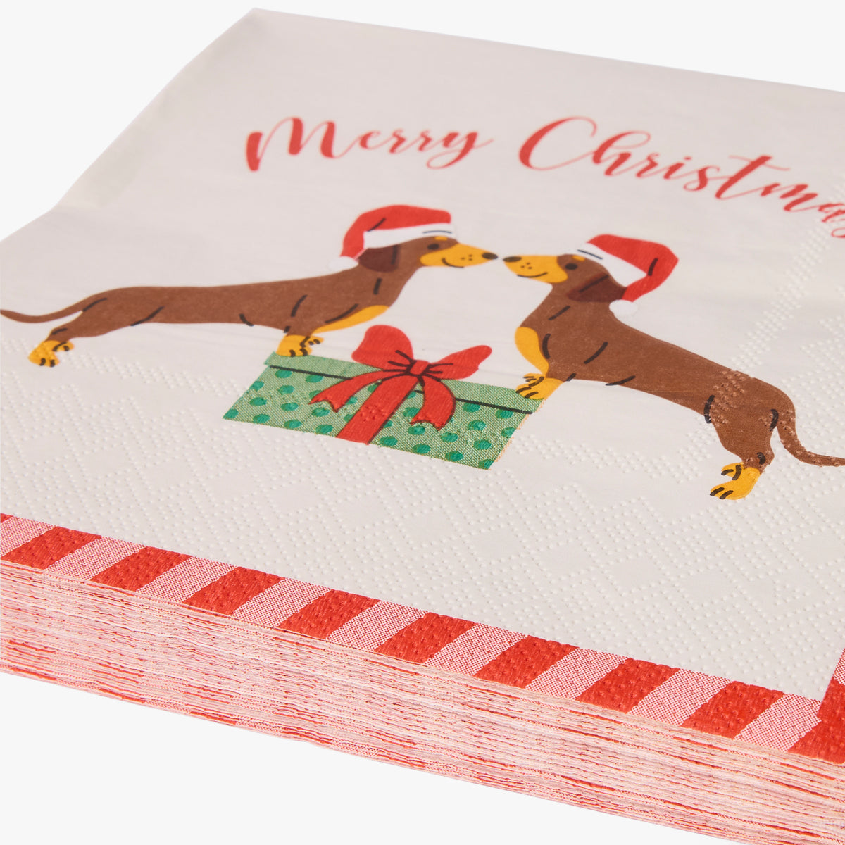 A stack of white paper napkins printed with a Christmas dachshund illustration and the words 'Merry Christmas' in red script. The napkins show two brown dachshunds wearing red Santa hats around a green gift box with a red bow.